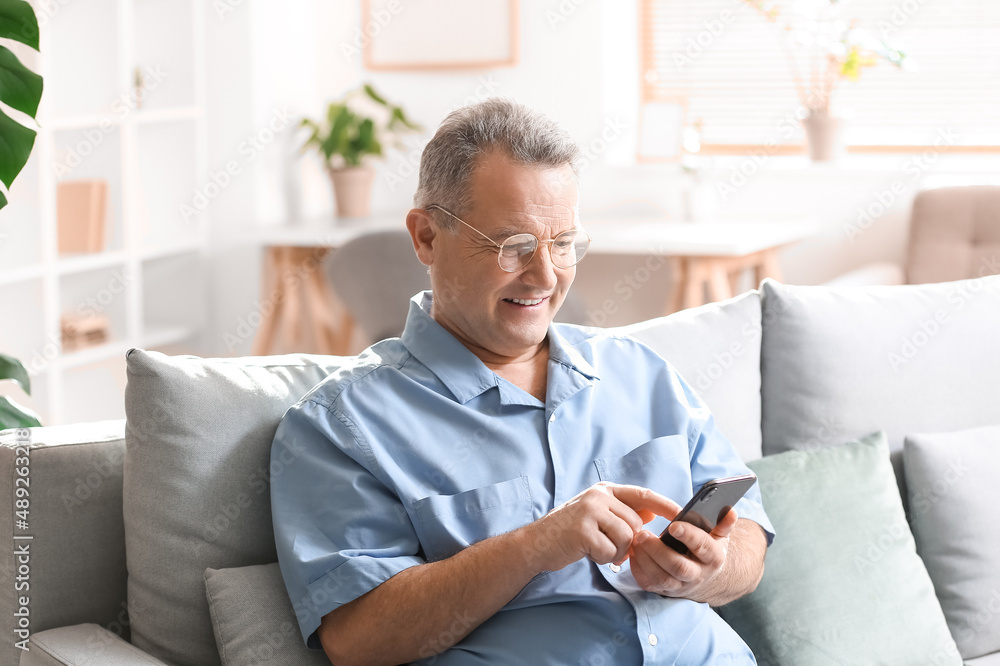 Sticker senior man in eyeglasses using mobile phone on sofa at home