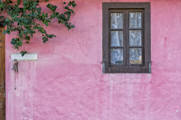 Fototapeta na wymiar Old house facade painted pink with a window and a branch of bougainvillea