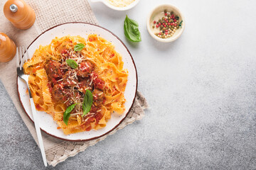 Tagliatelle pasta with meatballs in tomato sauce and thyme in sauce on light grey slate, stone or concrete background. Traditional Italian dish and cuisine. Top view with copy space.