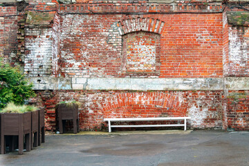 Old brick wall with a laid window next to a bench made of white wood and plants in stands