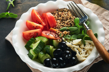 Vegetarian Vegan salad bowl or buddha bowl with tomato, cucumber, mozzarella cheese, quinoa, olives and microgreens. Healthy and balanced food concept on old wooden dark background Top view copy space