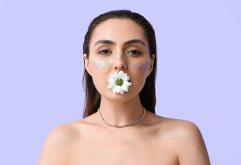 Beautiful woman with creative makeup holding daisy flower in mouth on color background