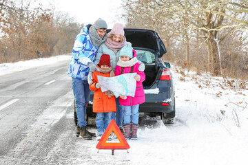 Parents and their little children with map near broken car on snowy winter day