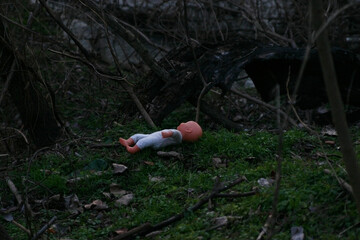 Baby doll forgotten lost in a dark forest laying on the ground; alone left behind; concept