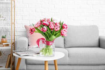 Bouquet of tulips, greeting card with text HAPPY WOMAN'S DAY and magazines on table in room
