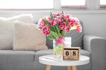 Cube calendar with date MARCH 8 and bouquet of tulips on table in light room. International Women's Day celebration