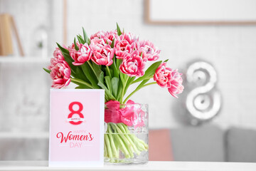 Vase with bouquet of beautiful tulips and greeting card with text HAPPY WOMEN'S DAY on table in light room