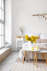 Vase with mimosa flowers, greeting card, decor and Easter eggs on table in bedroom