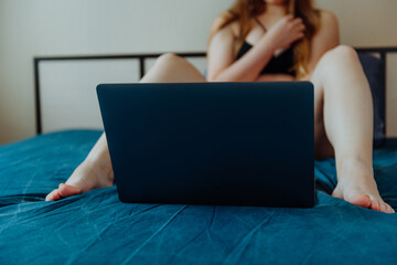 Webcam model. Young sexy woman using laptop on the bed. Flirting, online sex-chat, nudes concept.