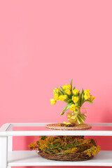 Vase with tulips and nest with Easter eggs on glass table near color wall