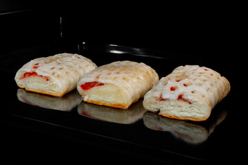Three puff pastry buns with red strawberry jam baking and rising on tray in electric oven. Homemade bakery, food, cooking and pastry concept