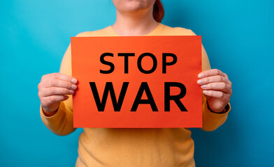 Closeup of young scared woman hands holding red poster banner with inscription Stop War, protesting on a blue background