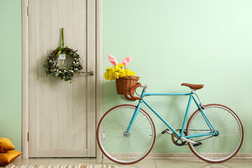 Bicycle with tulips and bunny ears near wooden door with Easter wreath in room