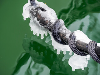  Close-up of a icy mooring rope with reflection in green colored water surface.