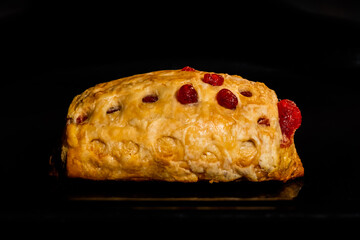 One baked puff pastry bun with red strawberry jam on tray in electric oven, black background - close up, side view. Bakery, food, cooking and pastry concept