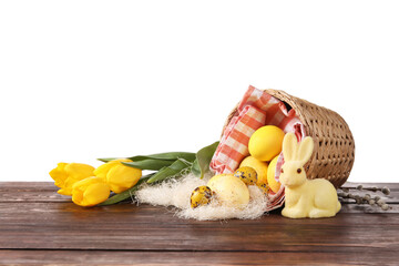 Basket with painted Easter eggs, tulip flowers and bunny on wooden table against white background