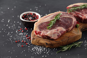 Raw beef steak on a cutting board with rosemary and spices.