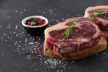 Raw beef steak on a cutting board with rosemary and spices.