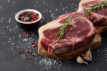Raw beef steak on a cutting board with rosemary and spices.