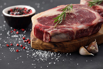 Raw beef steak on a cutting board with rosemary and spices.