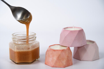 a spoon takes out berry cream-honey from a jar, a tower of candles in pink plaster candlesticks on a white background.