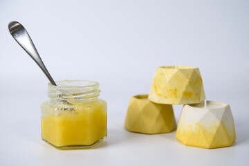 a spoon in a glass jar with honey and a tower of candles on a white background.