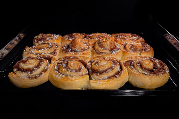 Twelve baked cinnamon buns on tray in electric oven - front view. Swedish cuisine, homemade bakery, food, cooking and pastry concept