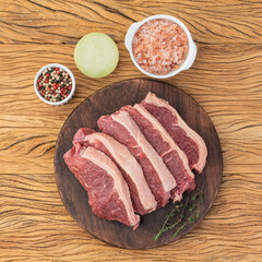 Sliced raw strip loin meat over wooden board with seasonings