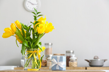 Vase with tulips and gift box on table in kitchen
