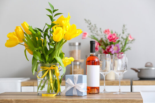 Vase with beautiful tulips, gift box, bottle of wine and glasses on table in kitchen