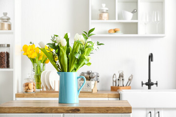 Jug with beautiful tulips and eucalyptus branches on kitchen counter