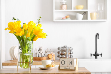 Vase with tulips, cup of coffee, macarons and cube calendar with date 8 MARCH in light kitchen. International Women's Day celebration