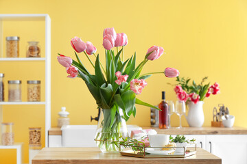 Vase with tulips, gift box, cup of coffee and macarons on table in kitchen