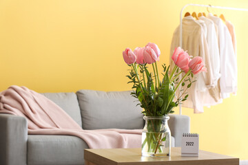 Glass vase with pink tulips and calendar on table in living room