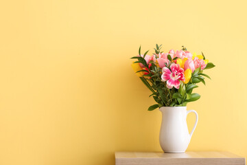 Vase with flowers on table near yellow wall