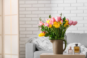 Vase with spring flowers and bottles of perfume on table in living room