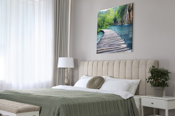 Canvas with printed photo of wooden bridge over lake and waterfall on beige wall in bedroom