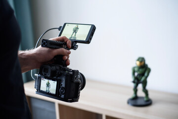 hold a camera with a camera monitor in your hands and take a video of a figure standing on a table