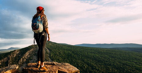 A lonely traveler with a backpack on the background of mountains, panorama. A female traveler in...
