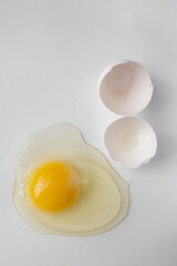 Broken egg with white and yolk spilled on the sides on white background