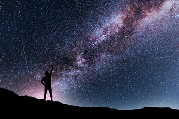 Silhouette of a person stands on the hill in starry night sky. Bright milky way galaxy behind him.