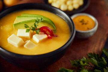 Ecuadorian locro de papa a traditional potato and cheese soup served with avocado and hominy. It’s on a wooden background - obrazy, fototapety, plakaty