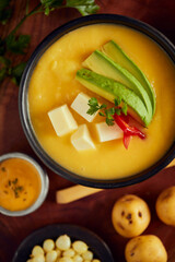 Ecuadorian locro de papa a traditional potato and cheese soup served with avocado and hominy. It’s on a wooden background