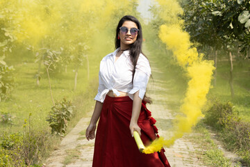 Happy Beautiful young girl woman bursting smoke bombs color smoke grenade cloud of dry color Holi...