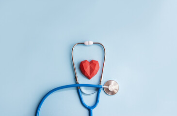 Medical stethoscope and red polygonal heart on a blue background. Minimal cardiology concept, copy space