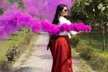 Happy Beautiful young girl woman playing holi bursting smoke bombs grenade color cloud of dry color...