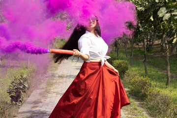 Fototapeta premium Holi festival of color Beautiful young girl woman in the park in spring break surround Multicolored smoke bombs color smoke grenade cloud of dry color Holi powder colour gulal abeer