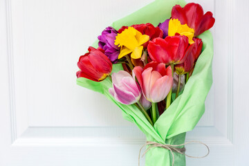 Bouquet of colorful tulips wrapped with green paper on white wooden  background 