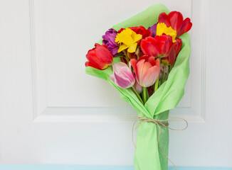 Bouquet of colorful tulips wrapped with green paper on white wooden  background 