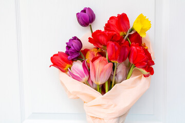Bouquet of colorful tulips wrapped with pink paper on white wooden  background 